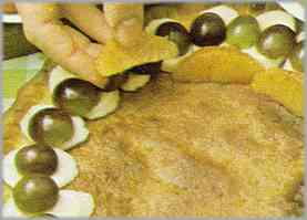 Comenzar a adornar la tarta con la fruta, formando círculos concéntricos y poniendo en el exterior los aros de plátanos con media uva encima de cada aro.